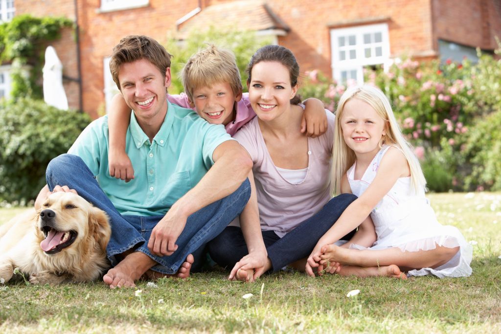 Family sitting on a lawn at home with their dog