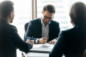 Three men in suits signing paperwork