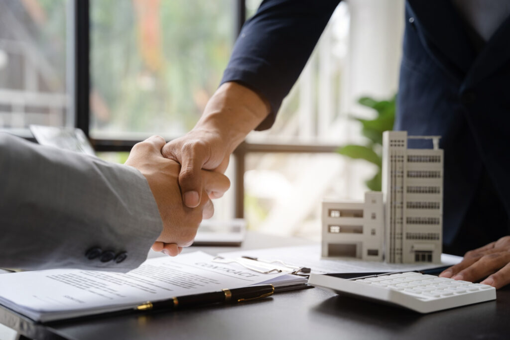 Two men shaking hands with contract on table