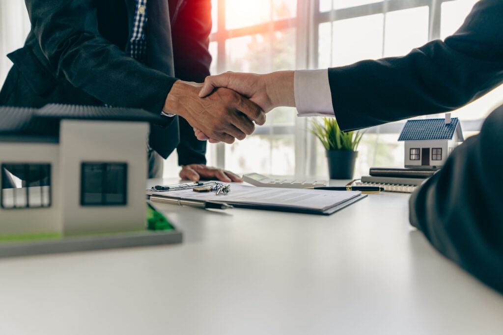 Men shaking hands at desk with paperwork and model house