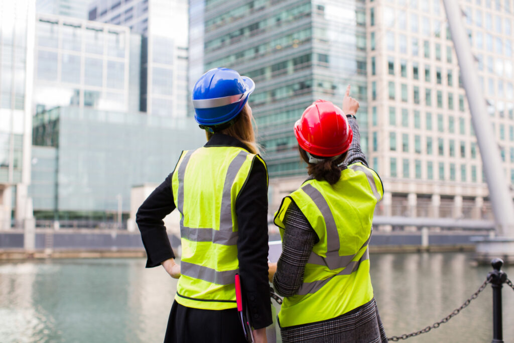 Two females in hard hats and high vis jackets pointing at high rise building